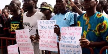 People hold signs during an anti-colonial demonstration against the regional CFA franc on the Place de l'Obelisque in Dakar on September 16, 2017. 
The CFA franc, which is pegged to the euro, is used in eight West African countries in the region, six of which are former French colonies. / AFP PHOTO / SEYLLOU